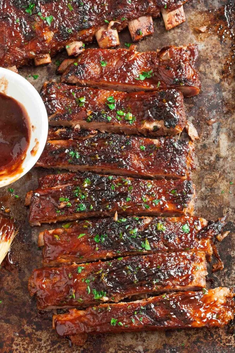 Overhead shot of a tray of cooked, glazed BBQ ribs garnished with herbs.