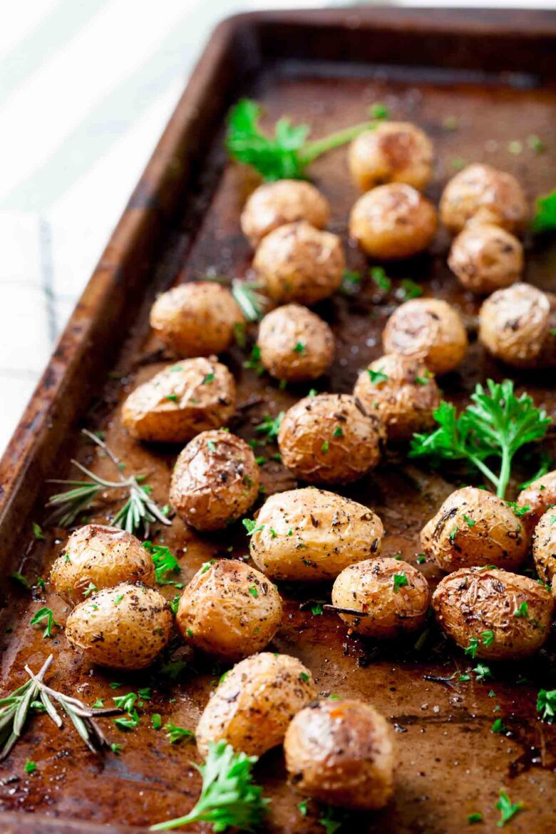 Roasted baby potatoes on a baking sheet, garnished with herbs like rosemary and parsley.