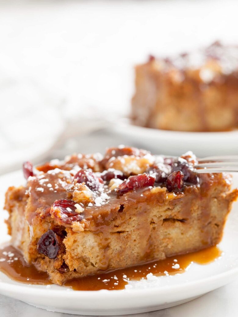 A slice of pumpkin bread pudding topped with caramel sauce and cranberries on a white plate.