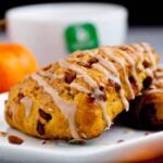 A close-up of glazed pumpkin scones on a white plate, studded with cinnamon and white chocolate chips.