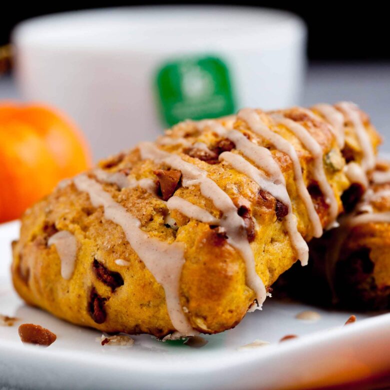 A close-up of glazed pumpkin scones on a white plate, studded with cinnamon and white chocolate chips.
