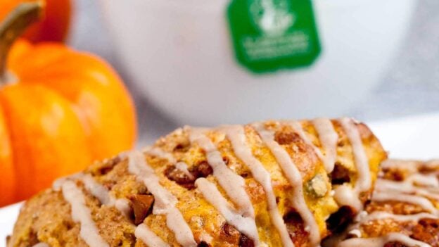 Pumpkin scones drizzled with icing on a white plate, with small pumpkins and a white mug in the background.