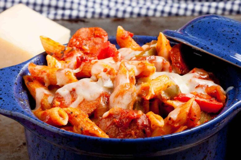 A blue dish filled with baked penne pasta topped with melted cheese, mixed with chunks of sausage and vegetables.