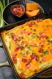 Overhead shot of creamy baked mashed potatoes with cheese and bacon bits on the side.