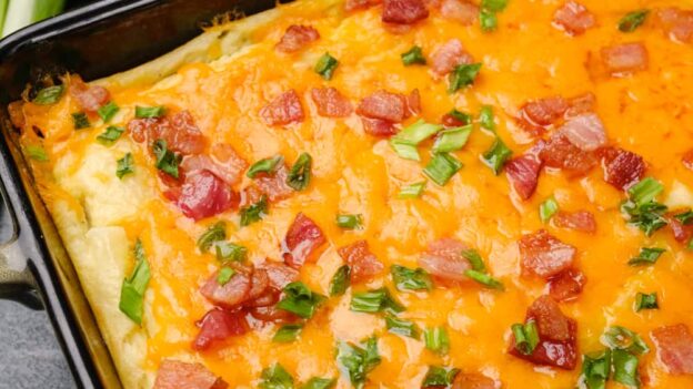 Overhead shot of creamy baked mashed potatoes with cheese and bacon bits on the side.