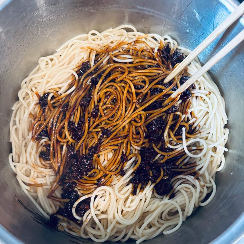 Dan dan noodle sauce being added to cooked noodles.