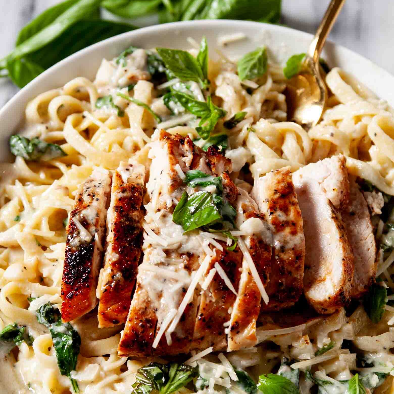 Closeup shot of a plate of healthy chicken Alfredo with sliced grilled chicken, fresh basil leaves, and grated cheese.