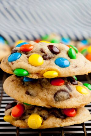 Closeup shot of three M&M Chocolate Chip Cookies stacked on top of each other on a wire rack.