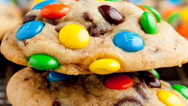Closeup shot of three M&M Chocolate Chip Cookies stacked on top of each other on a wire rack.