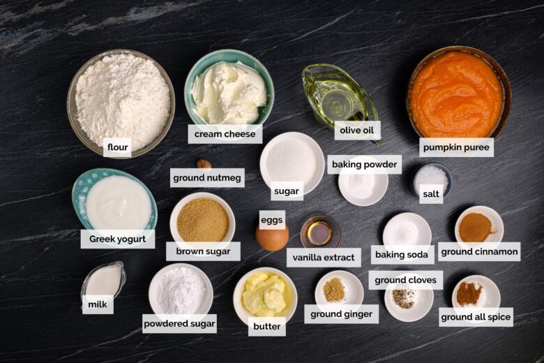 Overhead shot of ingredients to make pumpkin bundt cake with cream cheese frosting on a dark surface.