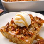 A slice of pumpkin bread pudding topped with vanilla ice cream and caramel sauce, served on a white plate.