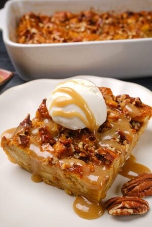 A slice of pumpkin bread pudding topped with vanilla ice cream and caramel sauce, served on a white plate.