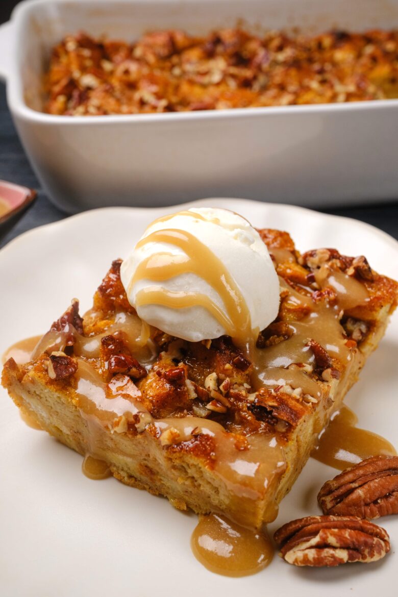 A slice of pumpkin bread pudding topped with vanilla ice cream and caramel sauce, served on a white plate.