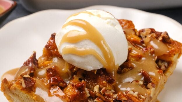 A slice of pumpkin bread pudding topped with vanilla ice cream and caramel sauce, served on a white plate.