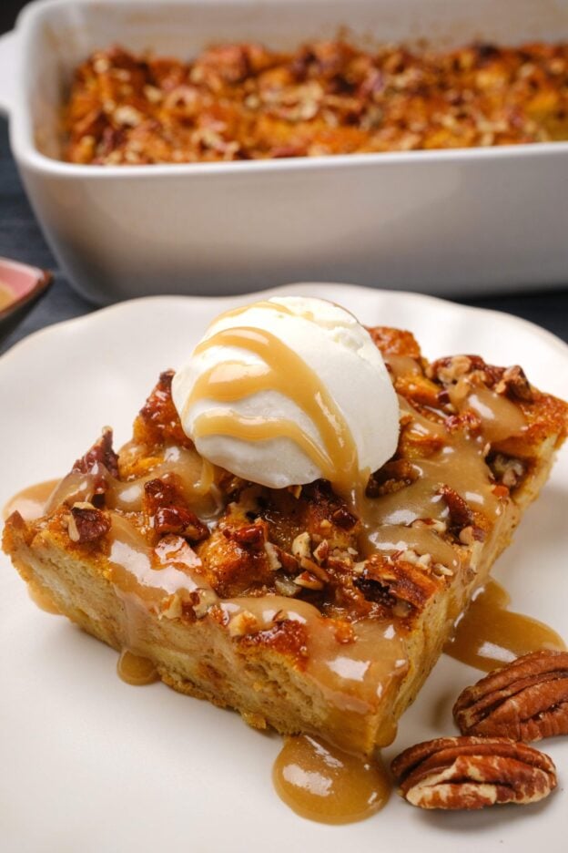 A slice of pumpkin bread pudding topped with vanilla ice cream and caramel sauce, served on a white plate.