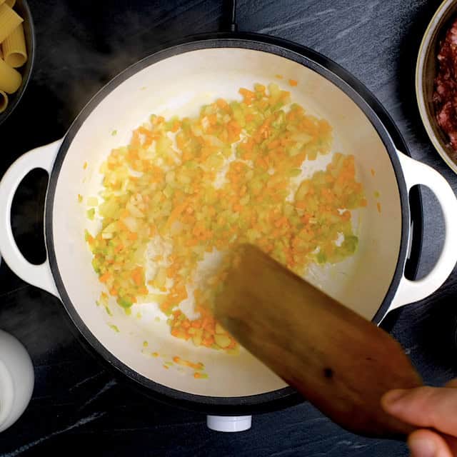Chopped onions, carrots, and celery being sautéed in a pot to make rigatoni bolognese.