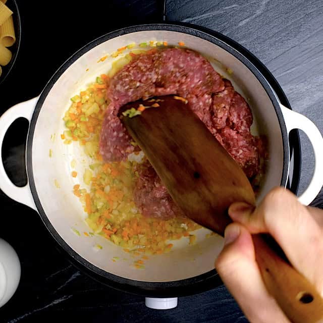 Ground beef being added to sautéed vegetable mixture to make rigatoni bolognese.