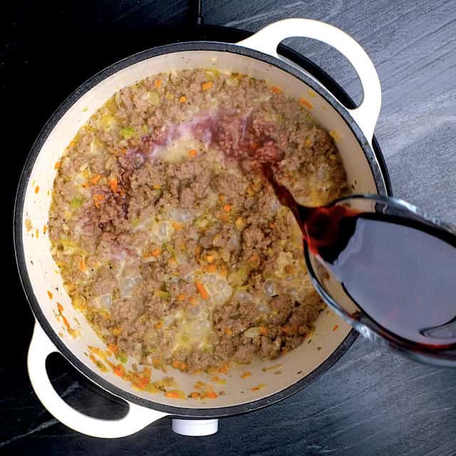 Red wine being added to ground beef and veggie mixture to make rigatoni bolognese.