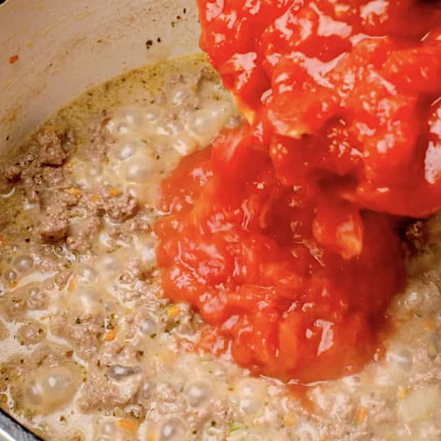 Chopped tomatoes being added to meat mixture to make rigatoni bolognese.