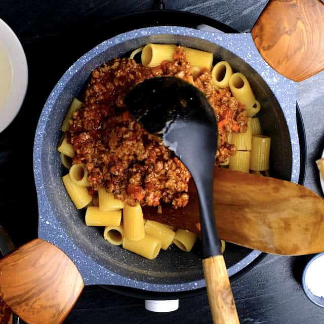Bolognese sauce being added to boiled rigatoni to make rigatoni bolognese.