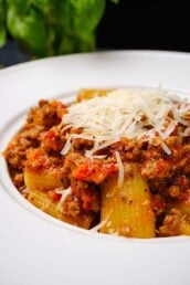 Closeup shot of homemade rigatoni bolognese with shredded cheese on top.