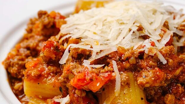 Closeup shot of homemade rigatoni bolognese with shredded cheese on top.