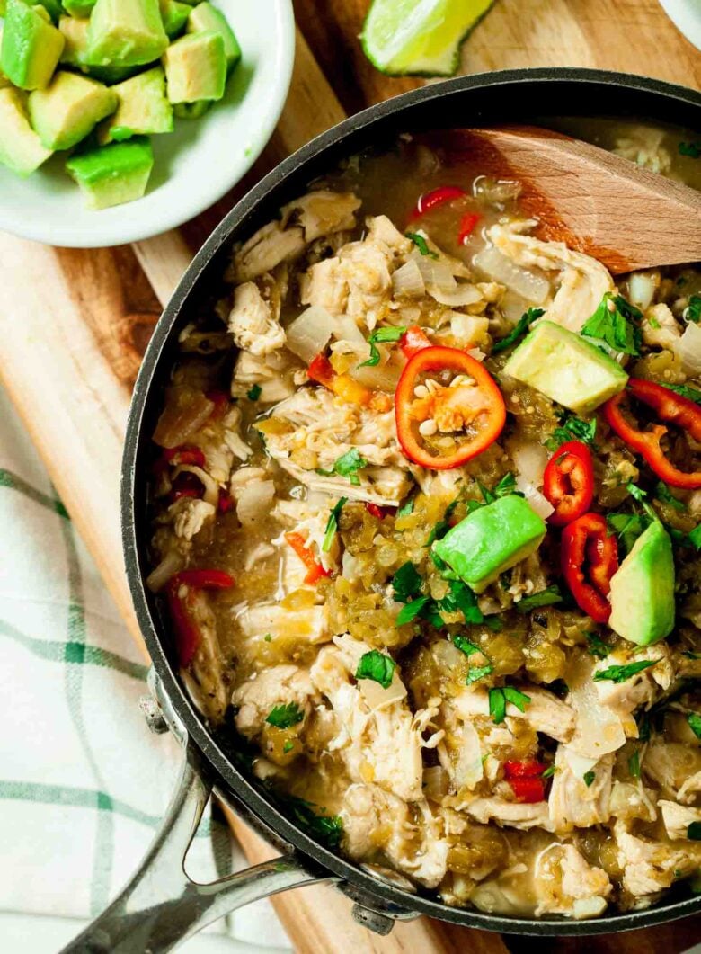 A skillet of freshly made Salsa Verde Chicken with shredded chicken, sliced red chilies, avocado cubes, and herbs.