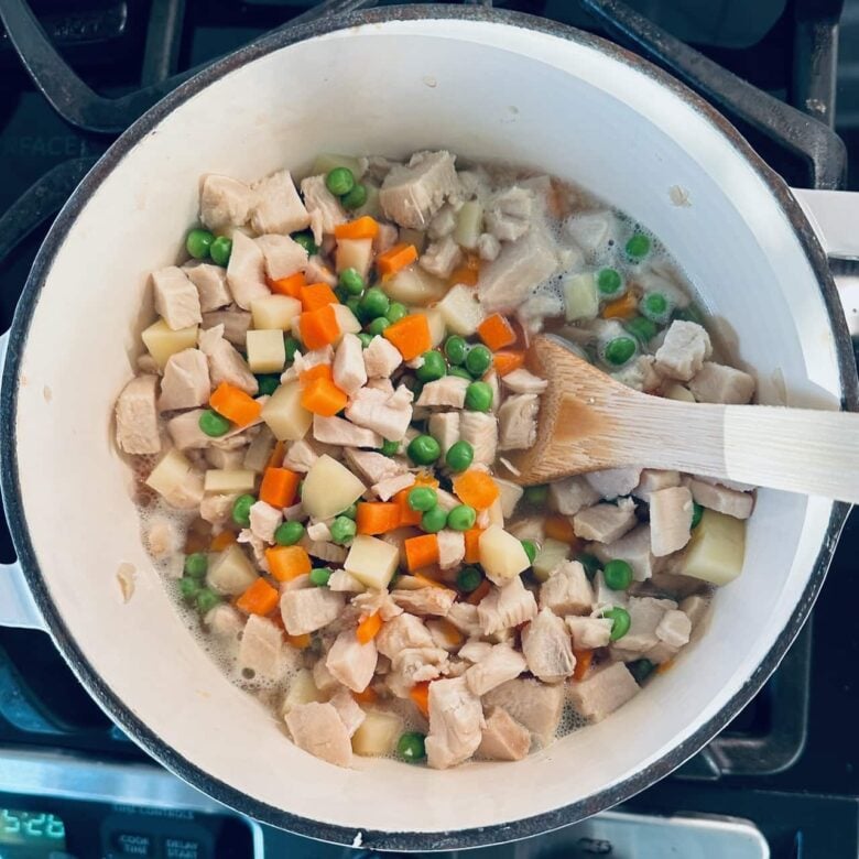 Overhead shot of pot with veggies and potato in a broth to make turkey pot pie.