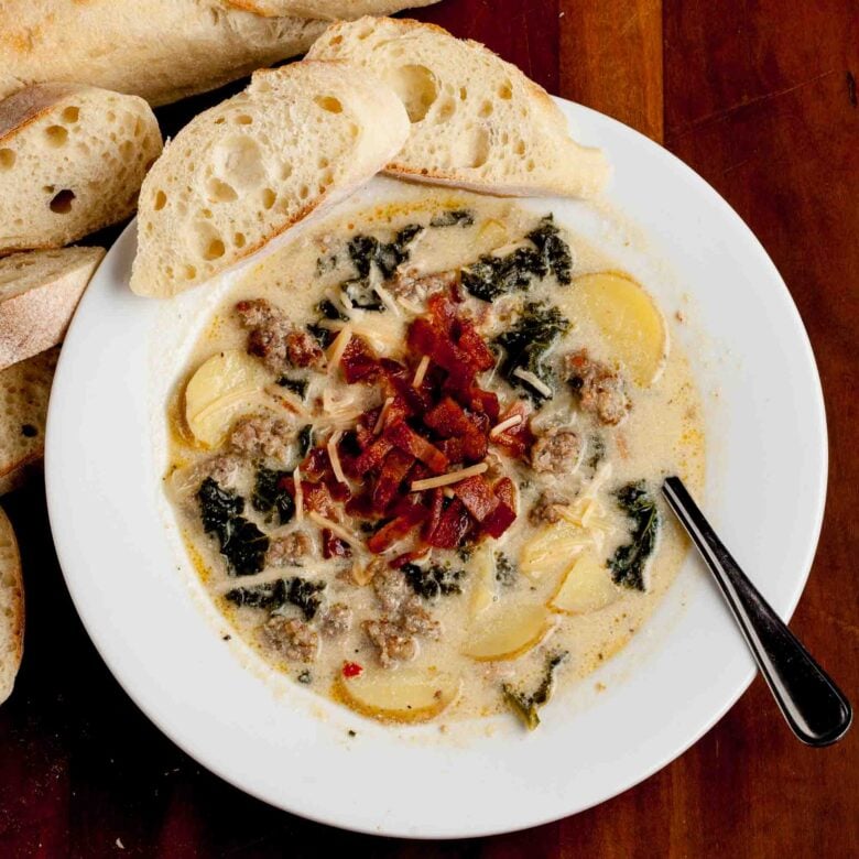 Overhead shot of homemade Zuppa Toscana soup, garnished with diced bacon and parmesan cheese with bread on the side.
