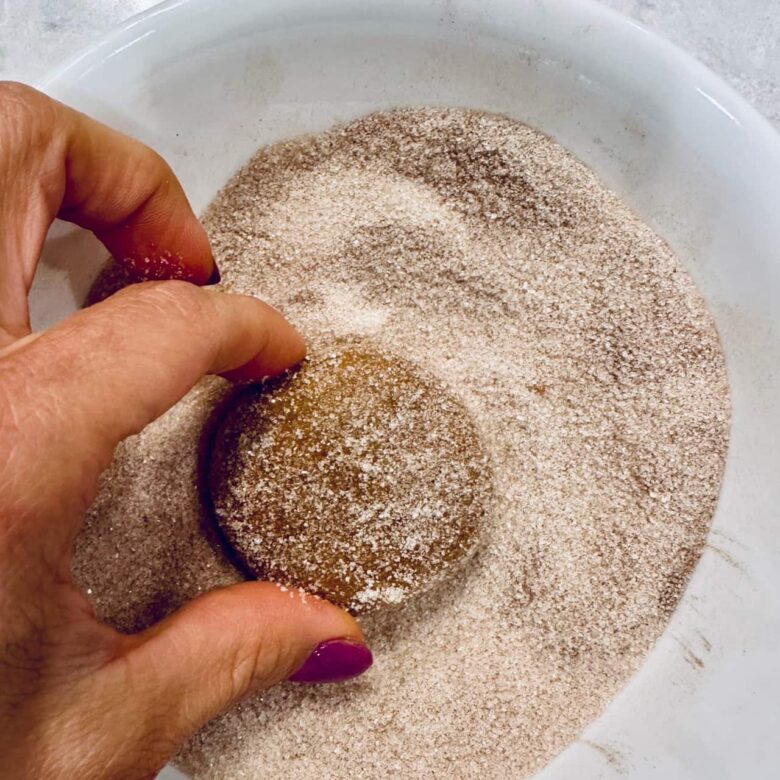 Flattened dough balls for pumpkin snickerdoodles being dipped in cinnamon-sugar coating.