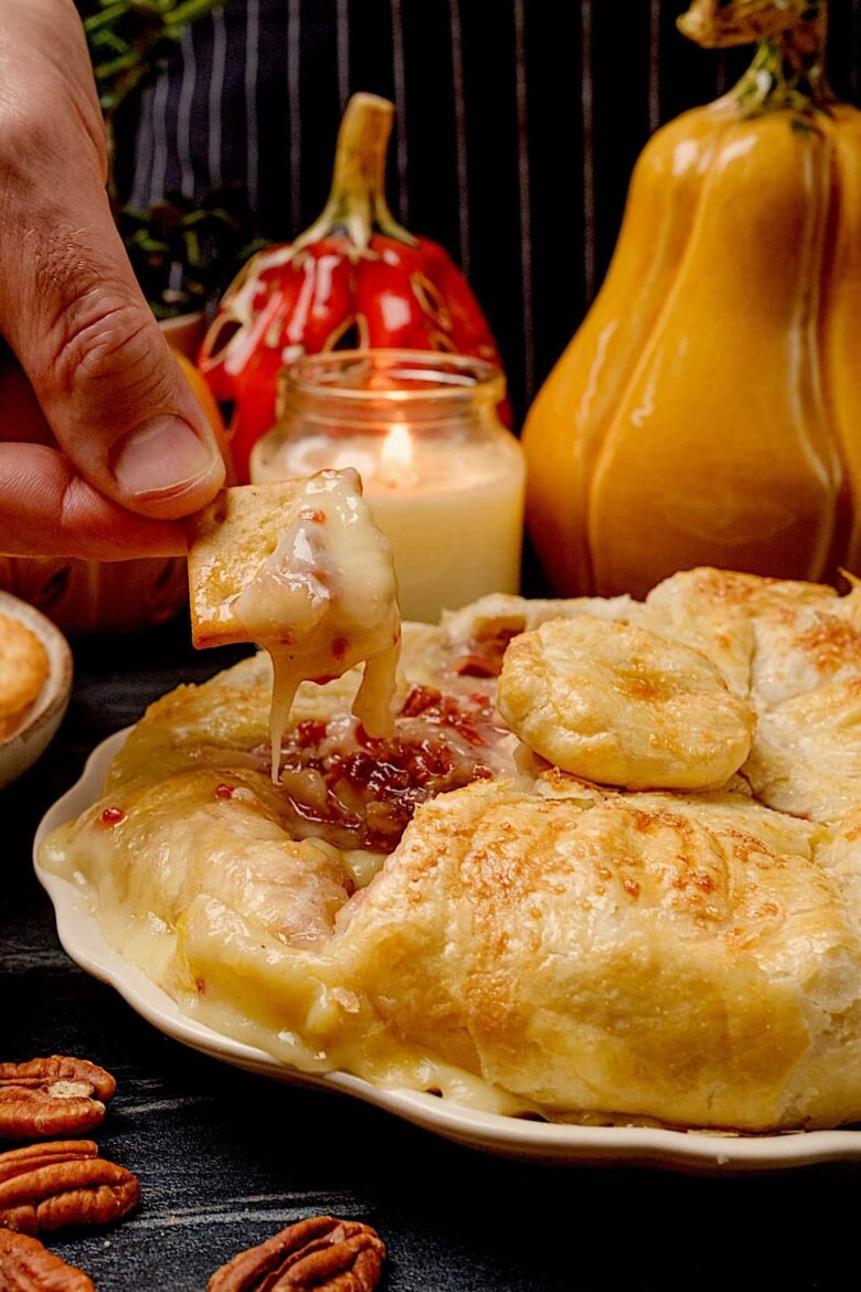 A person dips a cracker into melted brie en croute.
