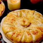 Baked brie en croute with golden crust on a white plate, accompanied by crackers.