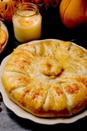 Baked brie en croute with golden crust on a white plate, accompanied by crackers.