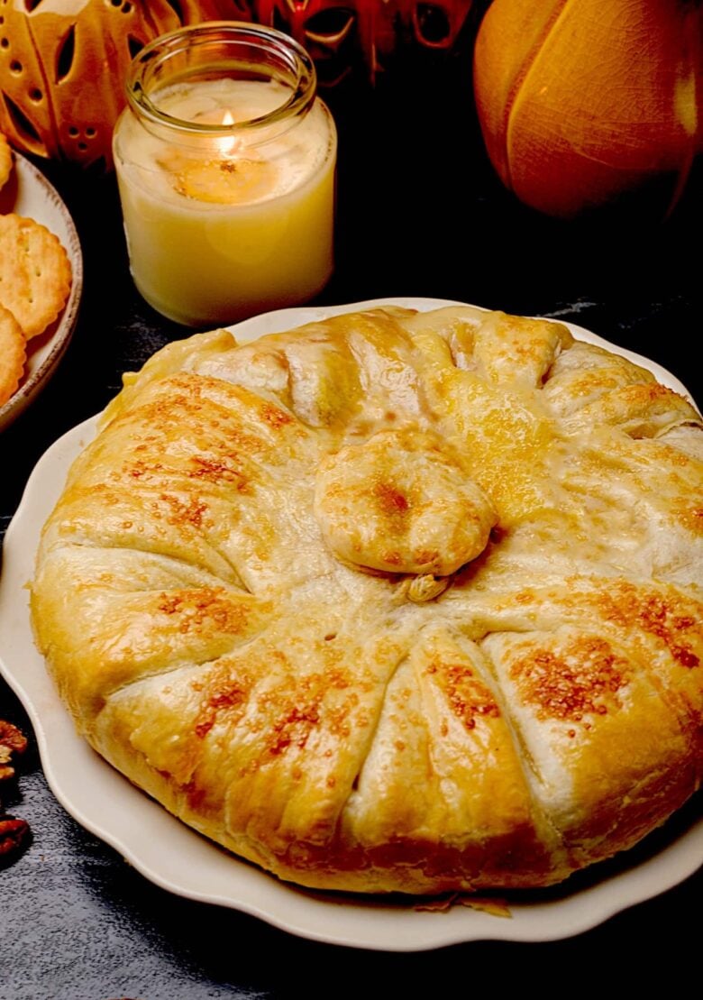 Baked brie en croute with golden crust on a white plate, accompanied by crackers.