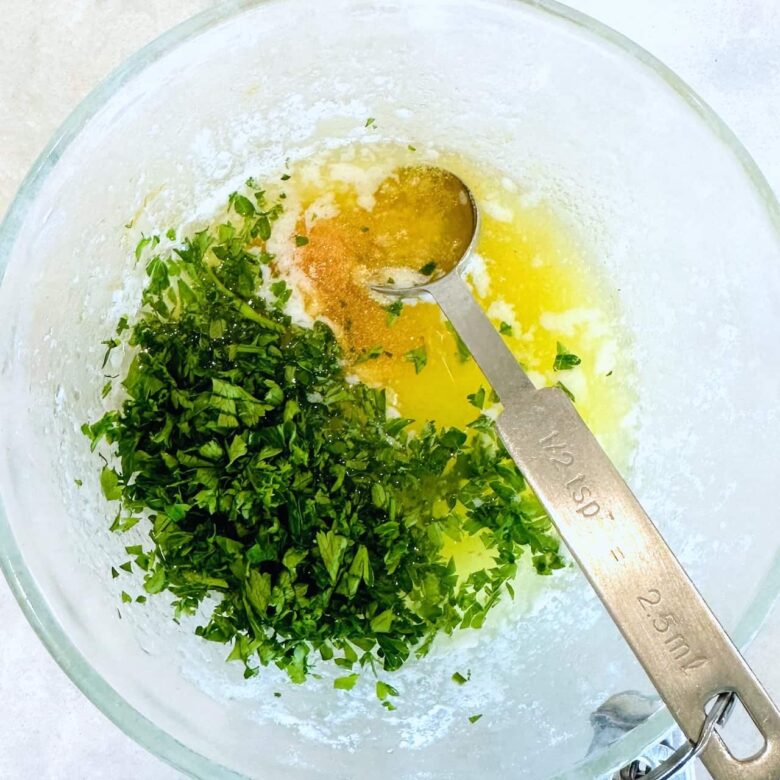 Melted butter and freshly chopped herbs in a glass bowl with a measuring spoon.