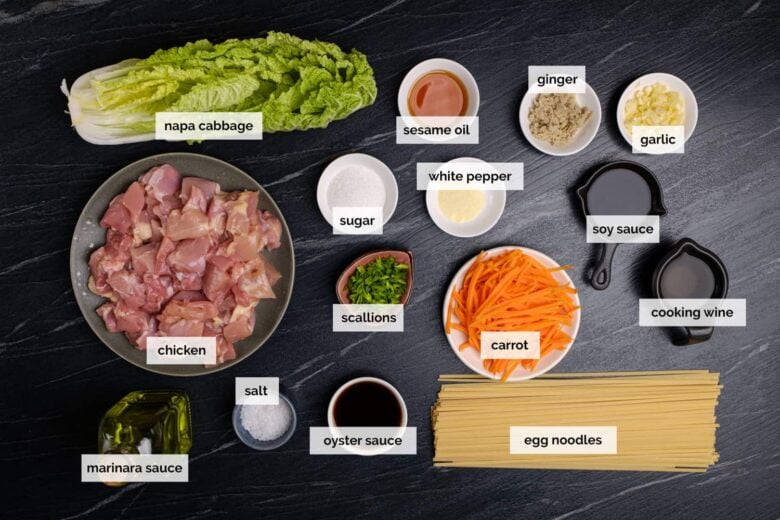 Overhead shot of ingredients to make chicken lo mein on a dark surface.