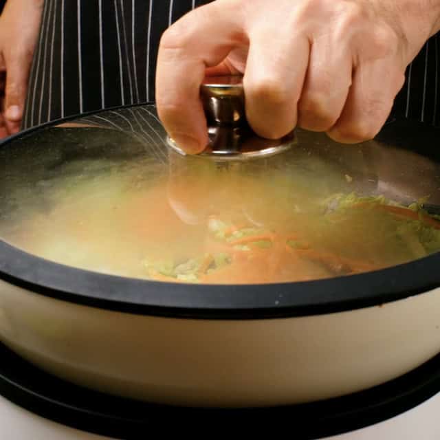 Cabbage and carrot mixture being covered with a lid to soften to make chicken lo mein.