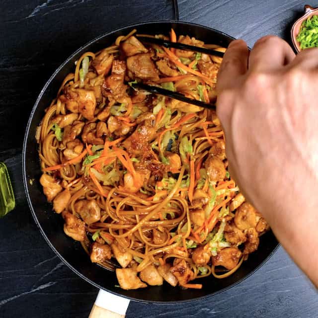 Stir fried chicken and vegetables being added to noodles to make chicken lo mein.