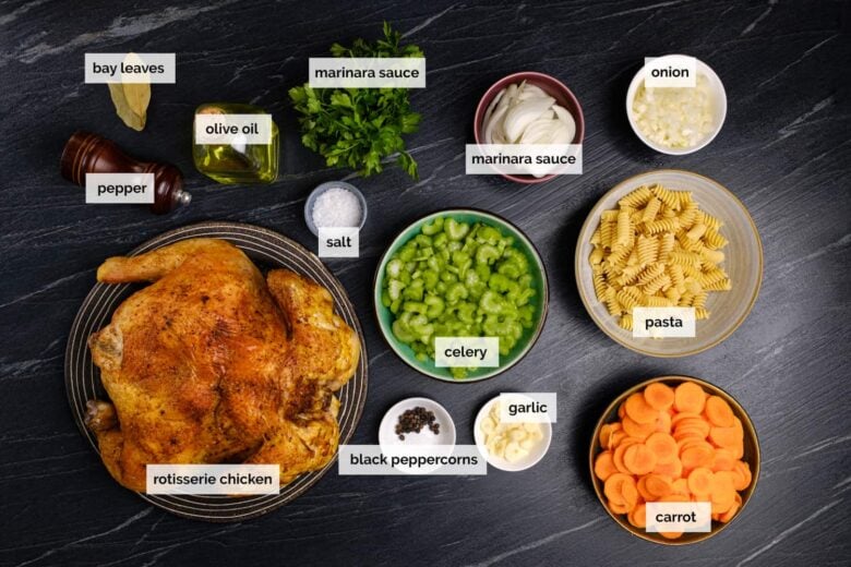 Overhead shot of ingredients to make homemade chicken noodle soup on a dark surface.