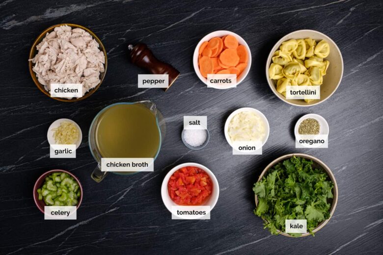 Overhead shot of ingredients to make chicken tortellini soup on a dark surface.