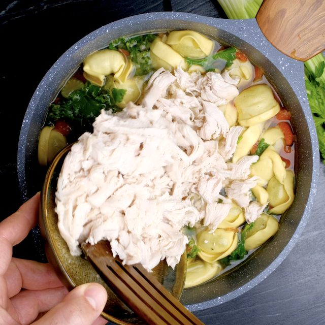 Shredded chicken being added to a pot with freshly made tortellini soup to make chicken tortellini soup at home.