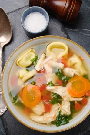 Overhead shot of a bowl of chicken tortellini soup with carrots, kale, and diced tomatoes.