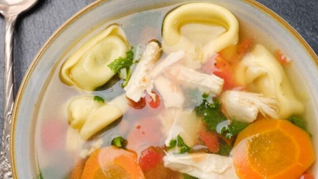 Overhead shot of a bowl of chicken tortellini soup with carrots, kale, and diced tomatoes.