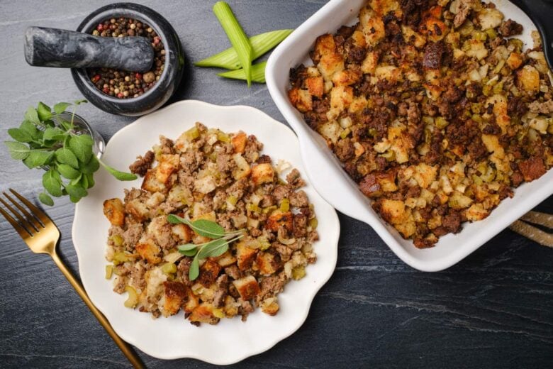 A plate and a baking dish filled with cornbread sausage stuffing, featuring cubed bread, ground meat, and vegetables.