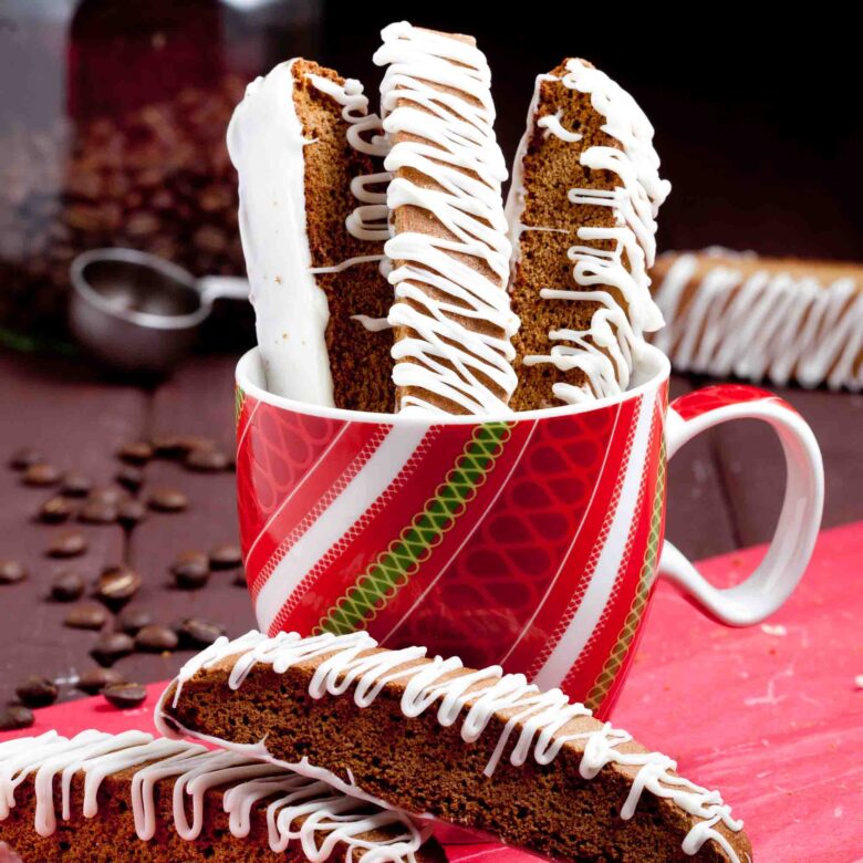 A festive mug holding multiple gingerbread biscotti drizzled with white chocolate.