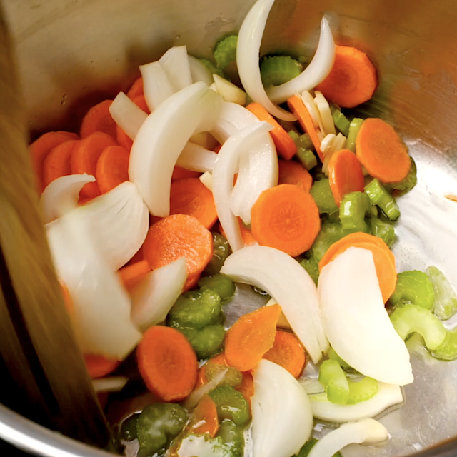 Vegetables being sautéed in a pot to make homemade chicken noodle soup.