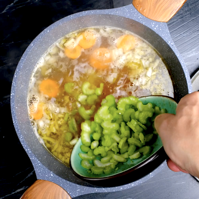 Vegetables being added to chicken broth to make homemade chicken noodle soup.