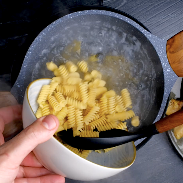 Rotini pasta being added to a pot to make homemade chicken noodle soup.
