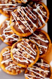 Close-up of stacked Rolo Pretzels topped with chocolate, chopped nuts, and white chocolate icing drizzle.