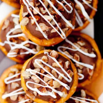 Close-up of stacked Rolo Pretzels topped with chocolate, chopped nuts, and white chocolate icing drizzle.